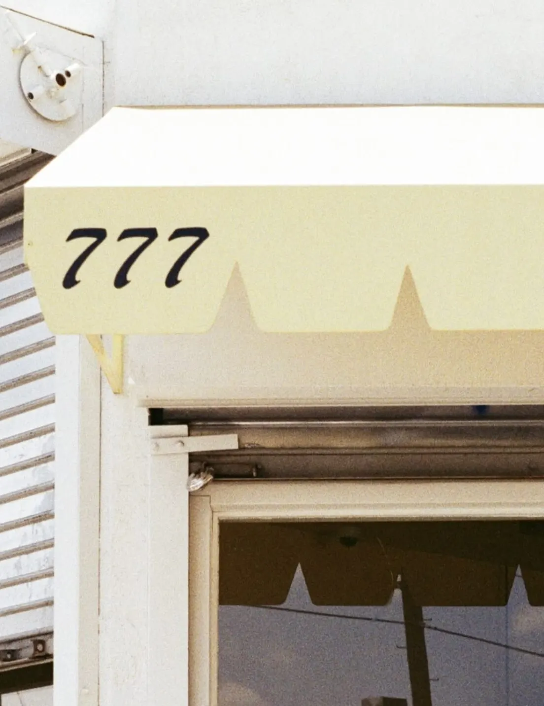 A pale yellow scalloped awning above a doorway, the number 777 painted on it.