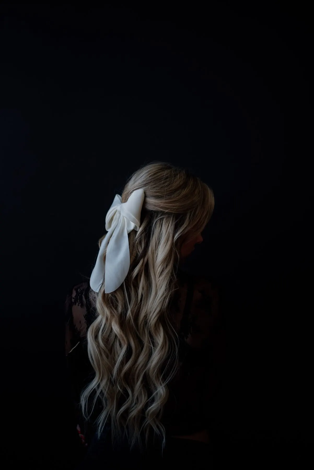 A dark frame — an ivory bow at the back of a dress, the woman turned away.