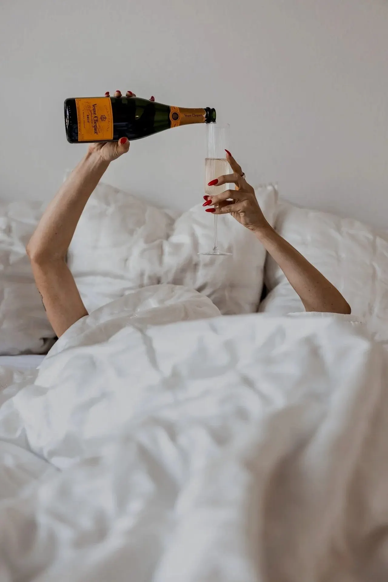 Champagne being poured into a glass held up from white bedding.