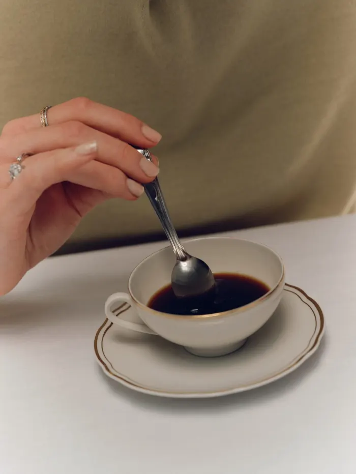 A hand stirring an espresso with a small spoon, shot tight.