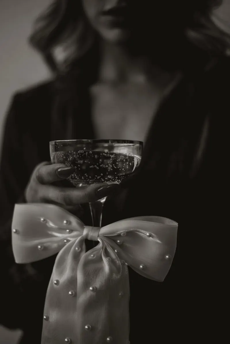 A champagne coupe held above a pearl-studded bow, shot close and low.