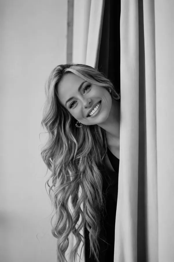 Tyler Tanner leaning out from behind a pale curtain, smiling, in black and white.