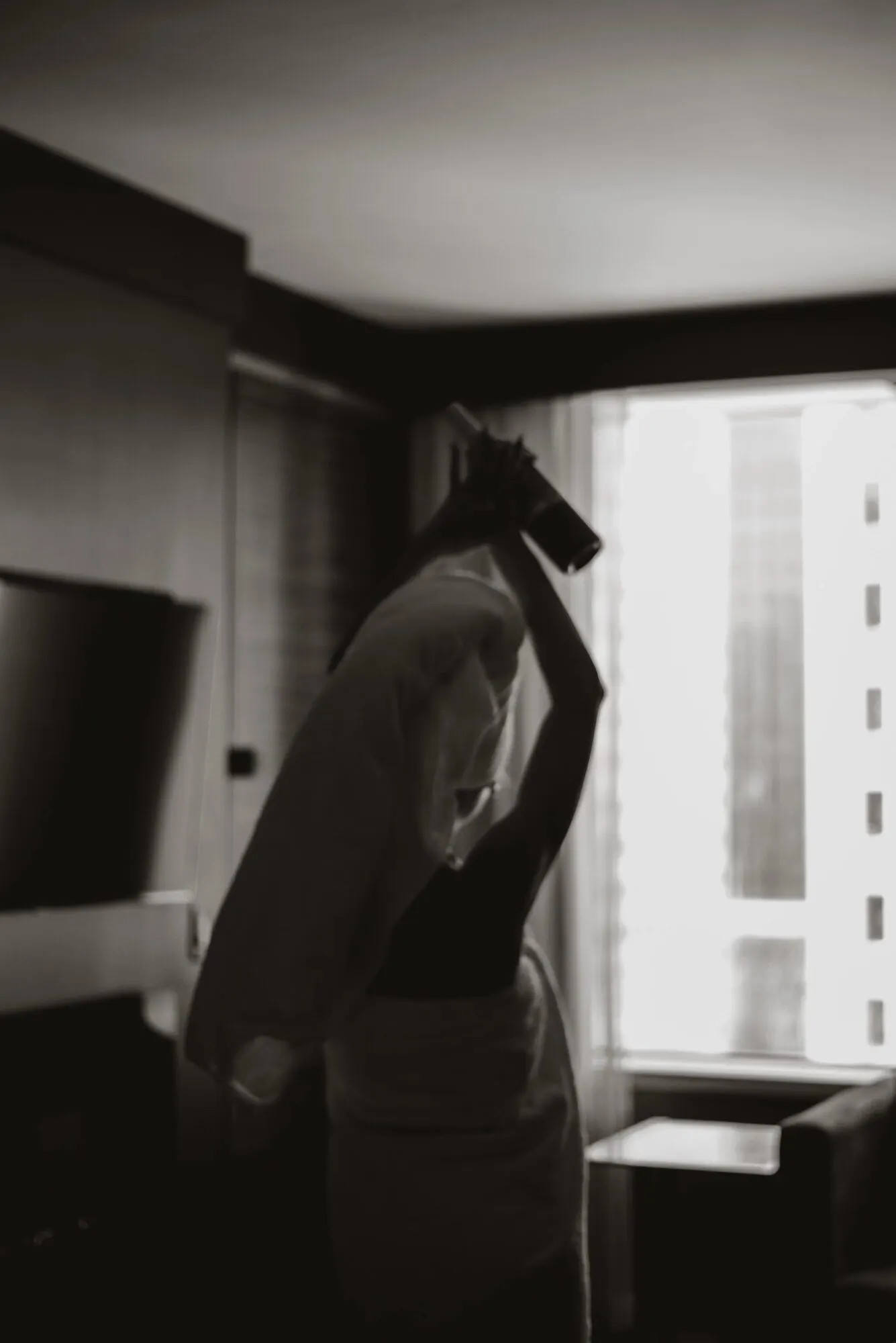 A dark interior with a single figure lit only by the window at the far end of the room.