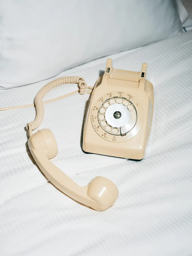 A rotary phone off the hook on a white bed.