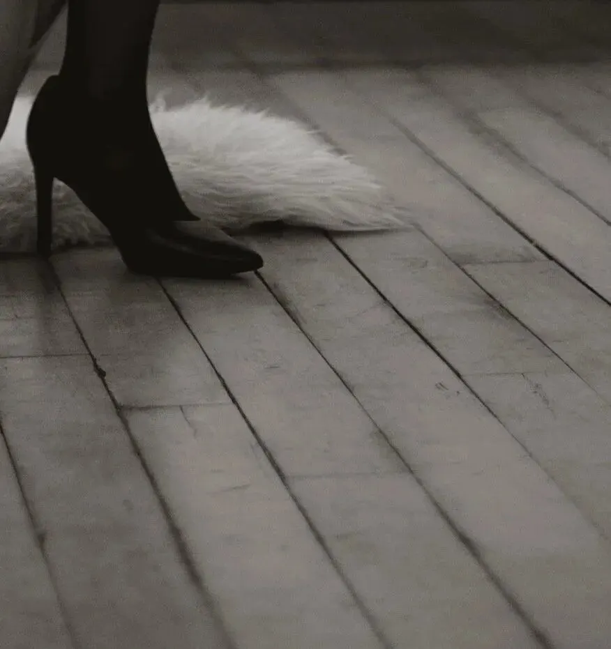 Close crop of a black heel on bare floorboards beside a pale fur.