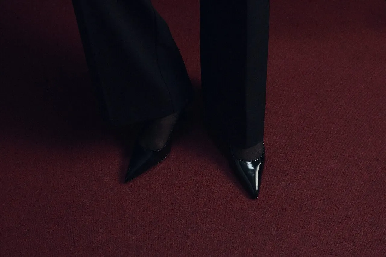Black boots standing on oxblood carpet, shot from above in a wide frame.