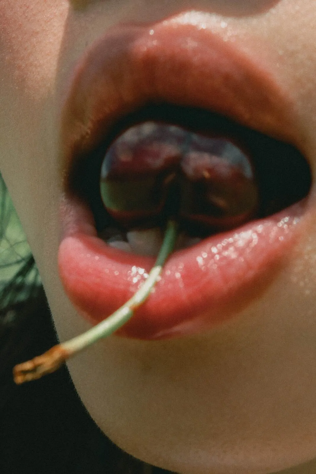 A cherry held between the teeth, close and dark.