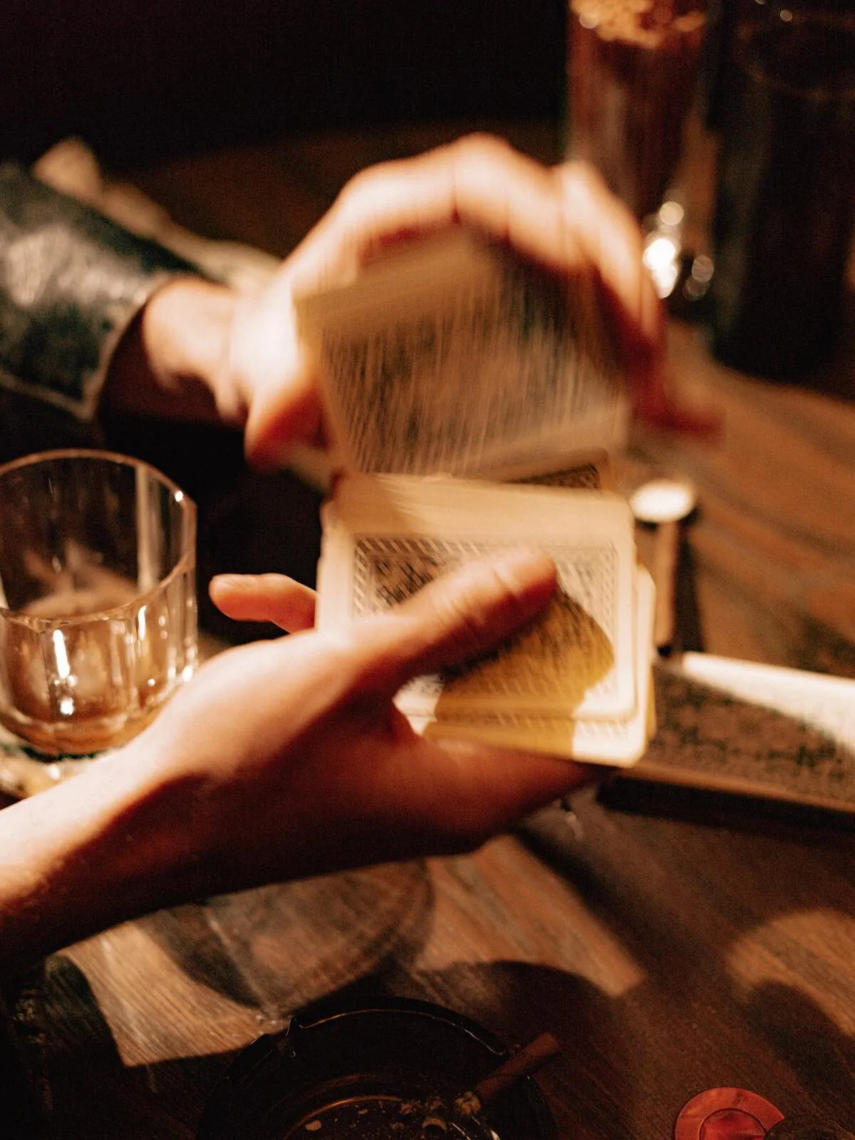 Two hands holding playing cards at a bar, low light.