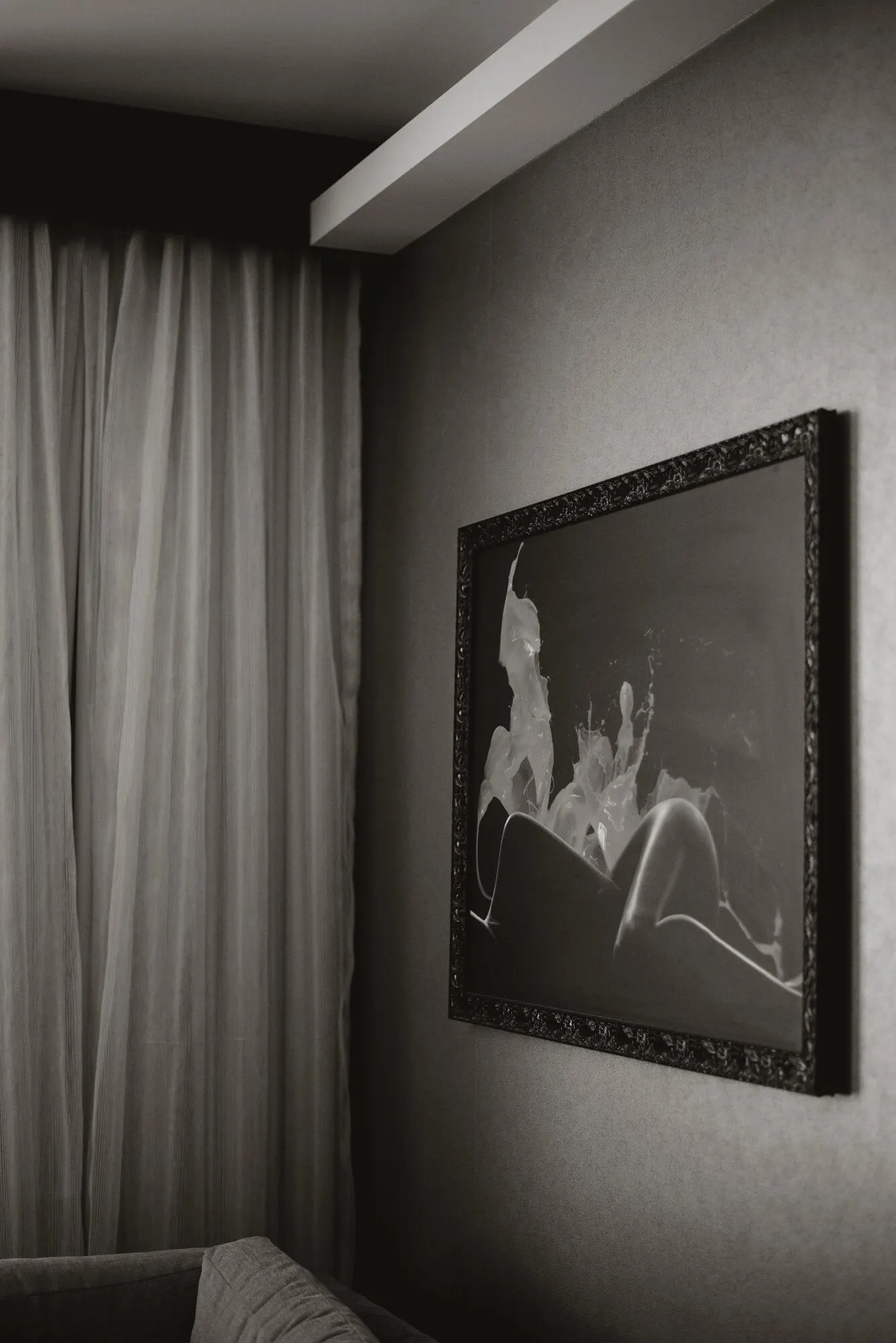A large framed photographic print on the wall of a low-lit hotel room, curtain edge in frame.