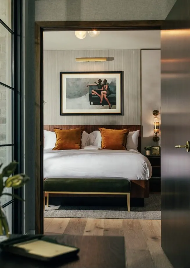 A dark, warmly lit hotel suite seen through the doorway — framed artwork, amber cushions, a made bed.