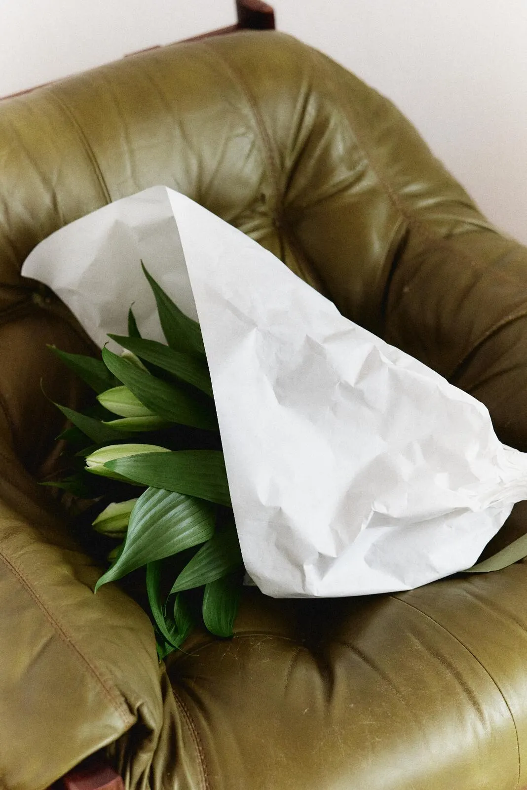 Wrapped lilies resting on an olive leather seat.