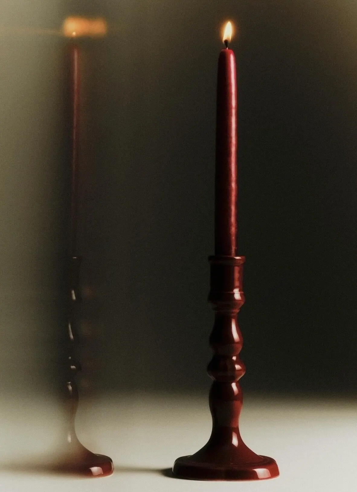 Two oxblood taper candles burning, filling the frame.