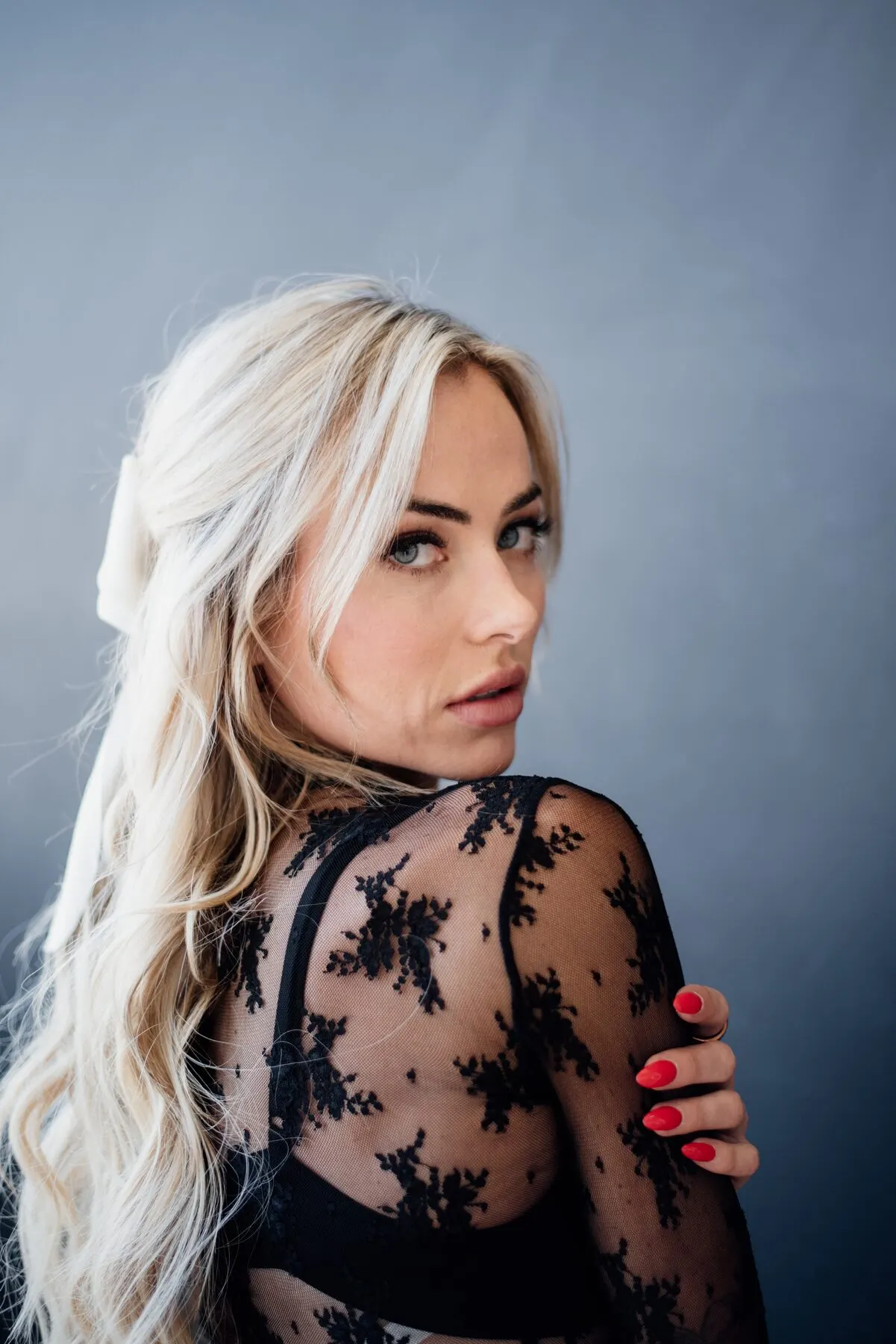 A woman in black lace with an ivory bow, looking back over her shoulder, red nails.
