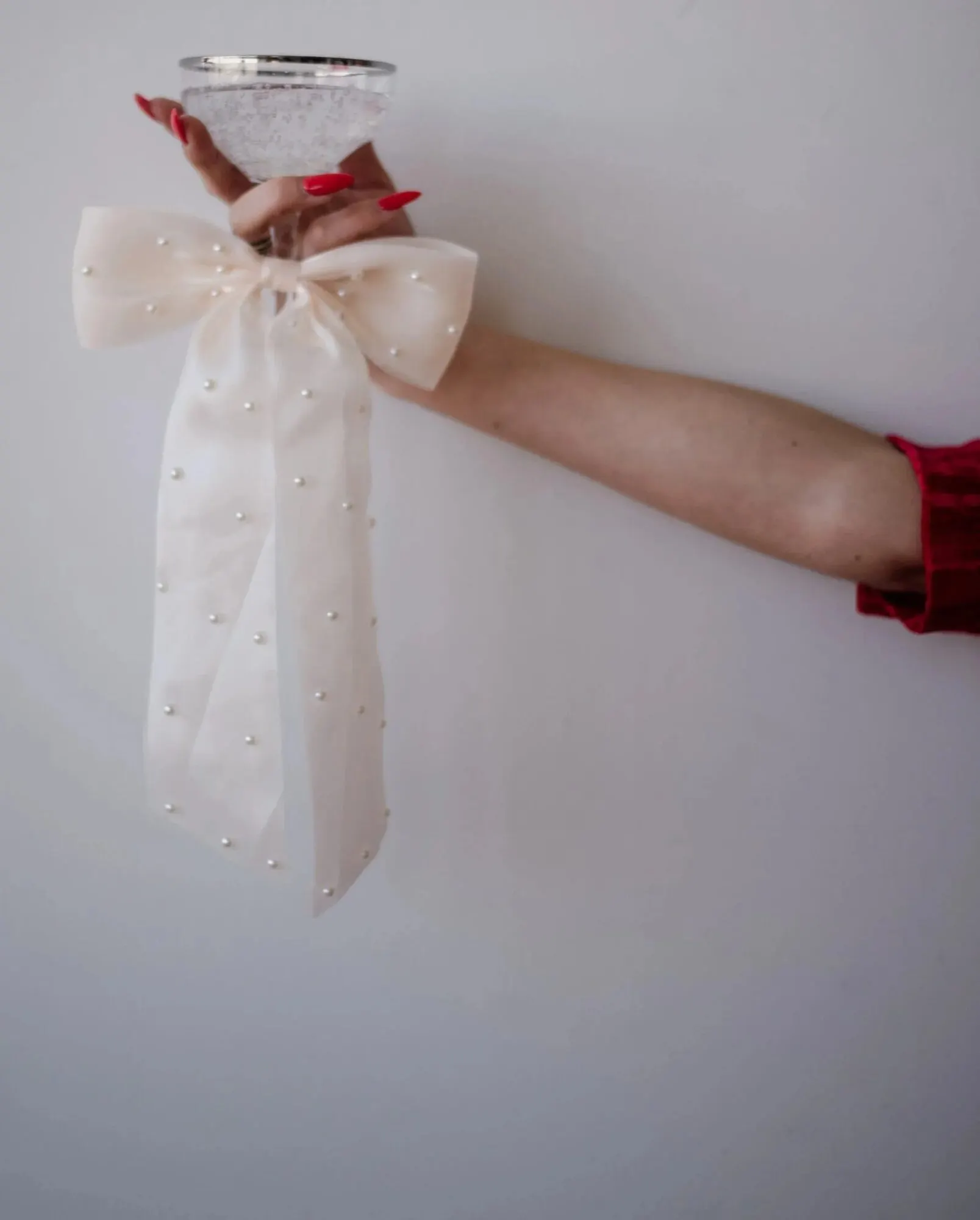 A pearl-studded tulle bow held against a pale wall.