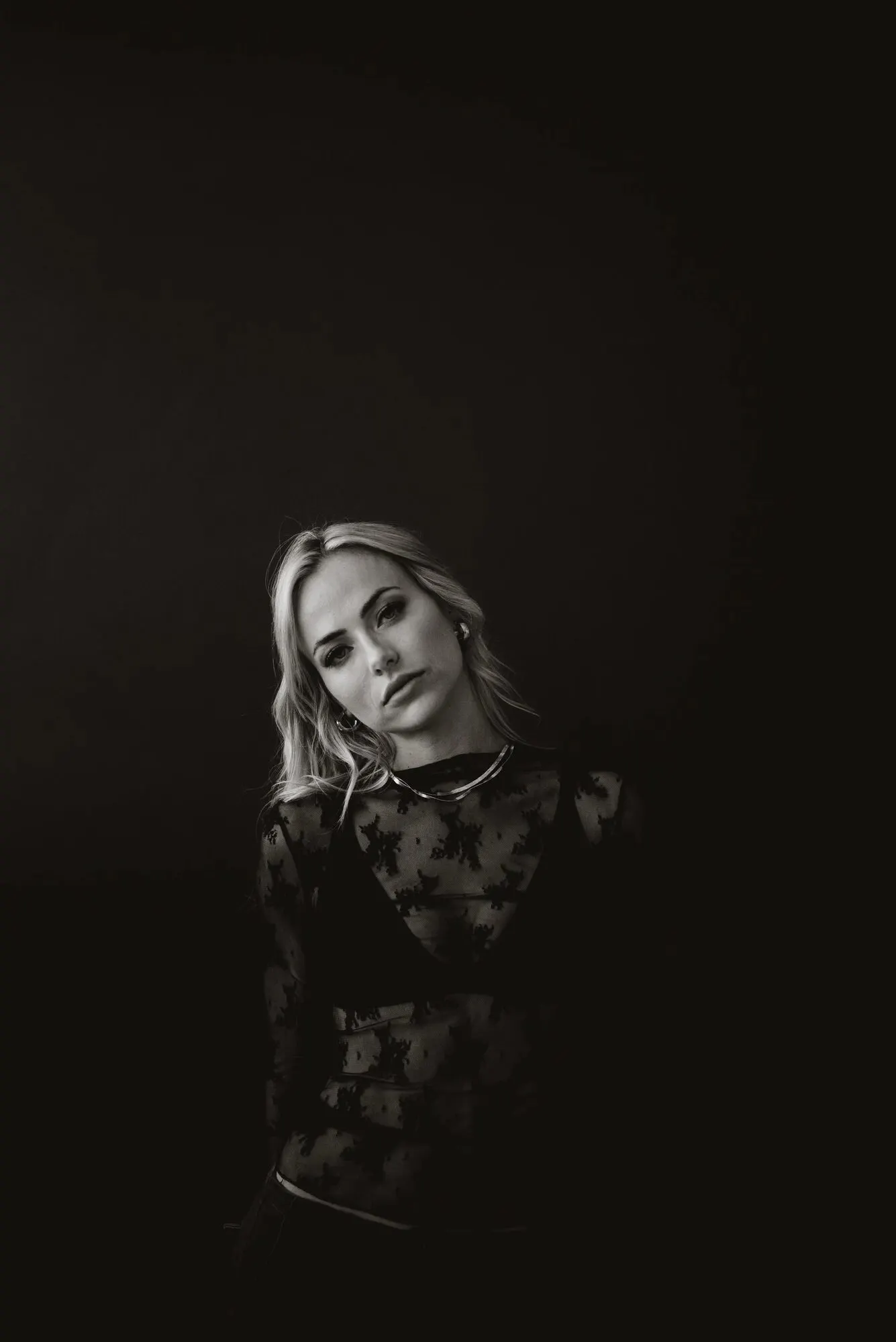 Low-key black-and-white portrait of Tyler Tanner in black lace against near-black, only her face and one shoulder lit.