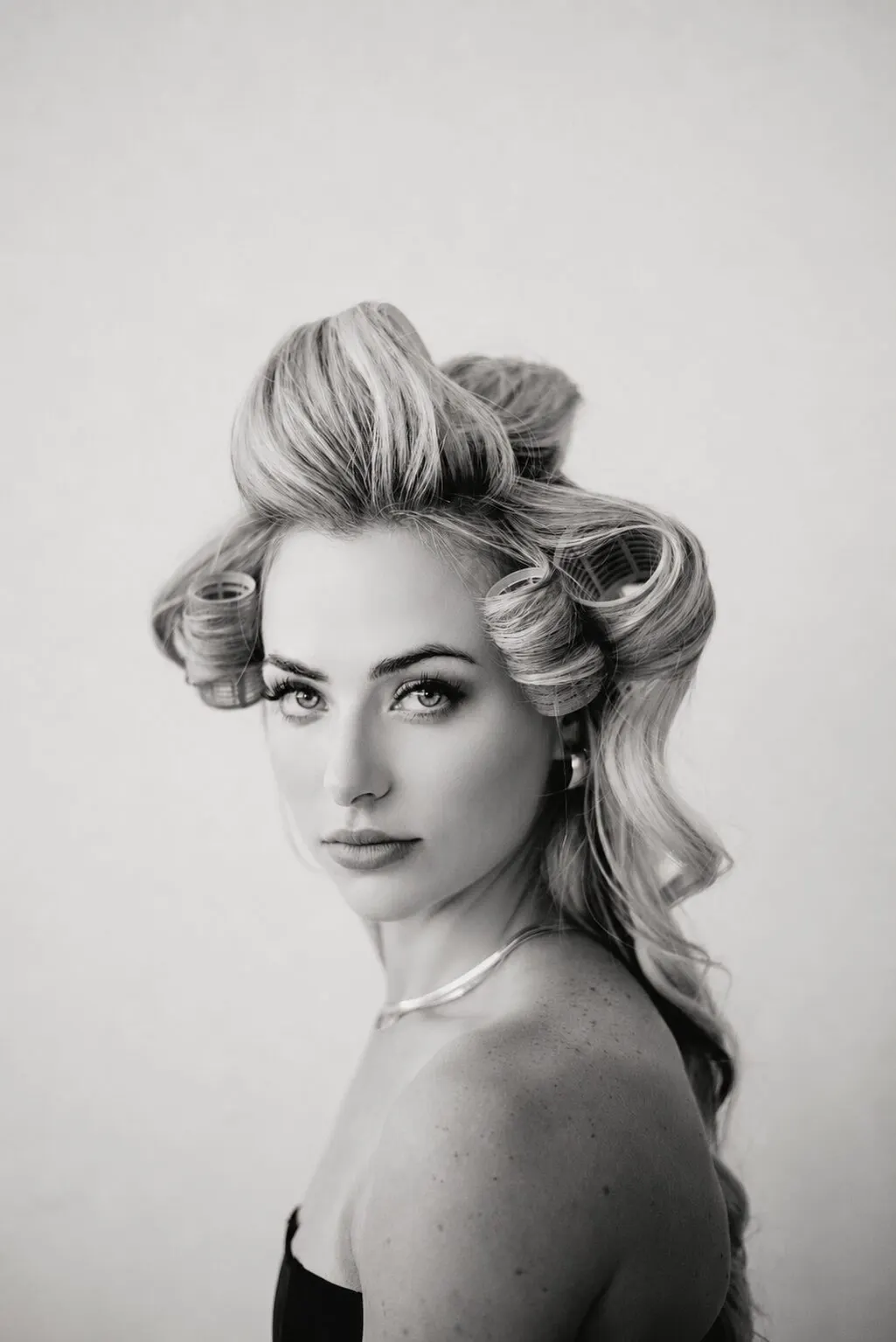 Beauty portrait with pinned set hair, shoulders bare, shot against pale grey.